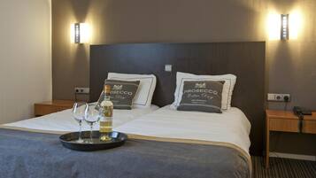 Ein Hotelzimmer mit einem großen Bett, zwei Nachttischen, einem Tablett mit Flasche und Gläsern sowie zwei Wandlampen.