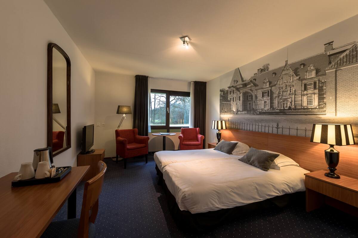Una habitación de hotel con una cama grande, un escritorio con lámpara, una silla, un televisor y una ventana con cortinas.