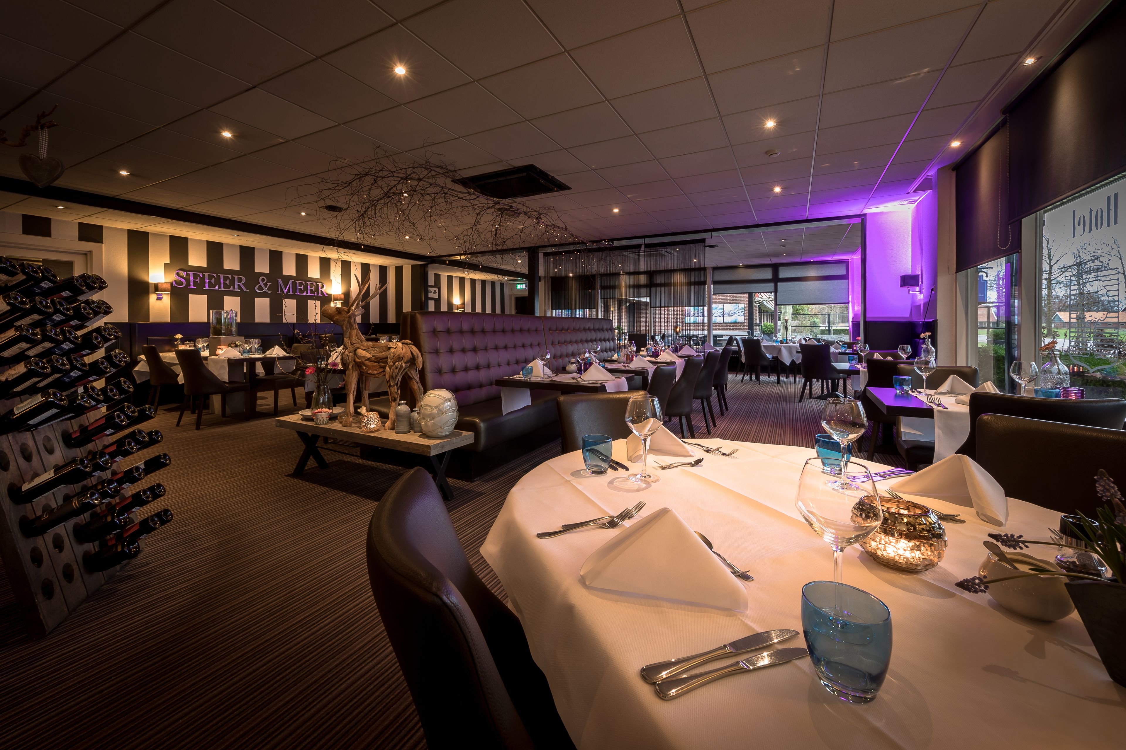 A restaurant with a bar area, tables set for dining, and a wine rack.