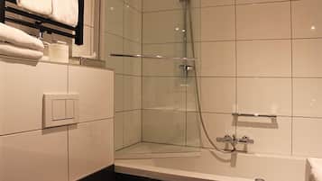 A modern bathroom with a glass shower enclosure, a bathtub, and a towel rack with towels.