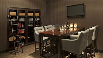 Un comedor con una mesa de madera, seis sillas tapizadas, una estantería con botellas de licor y un televisor montado en la pared.