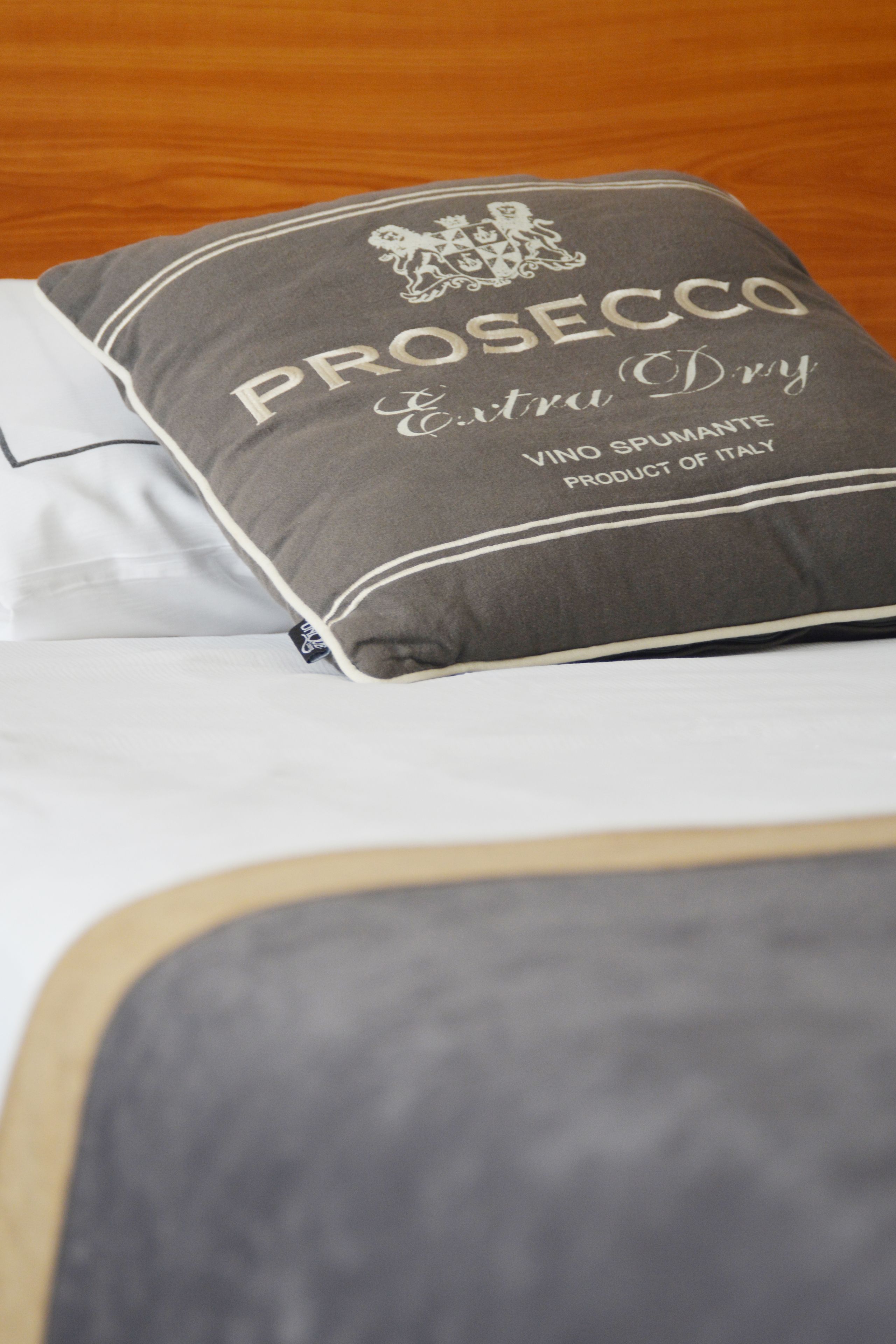 A bed with a pillow labeled "PROSECCO Extra Dry" and a tag indicating it is a product of Italy.
