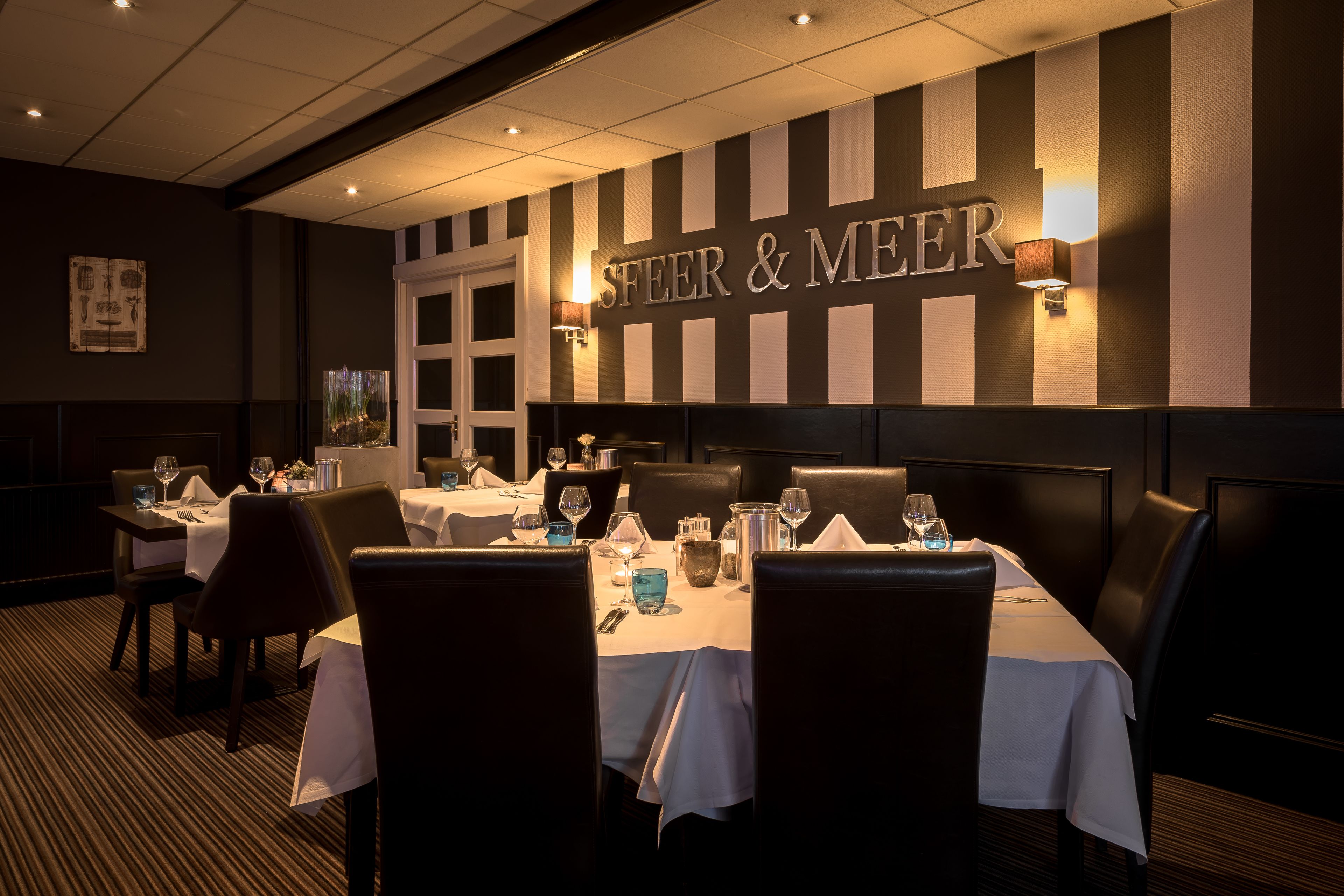 A restaurant interior with striped walls, tables set with white tablecloths, and candlelit ambiance.