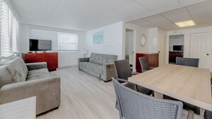 A spacious living area with a large wooden table and several chairs, a grey sofa, and a television on a red cabinet. - Alante Oceanfront Motel (North Wildwood)