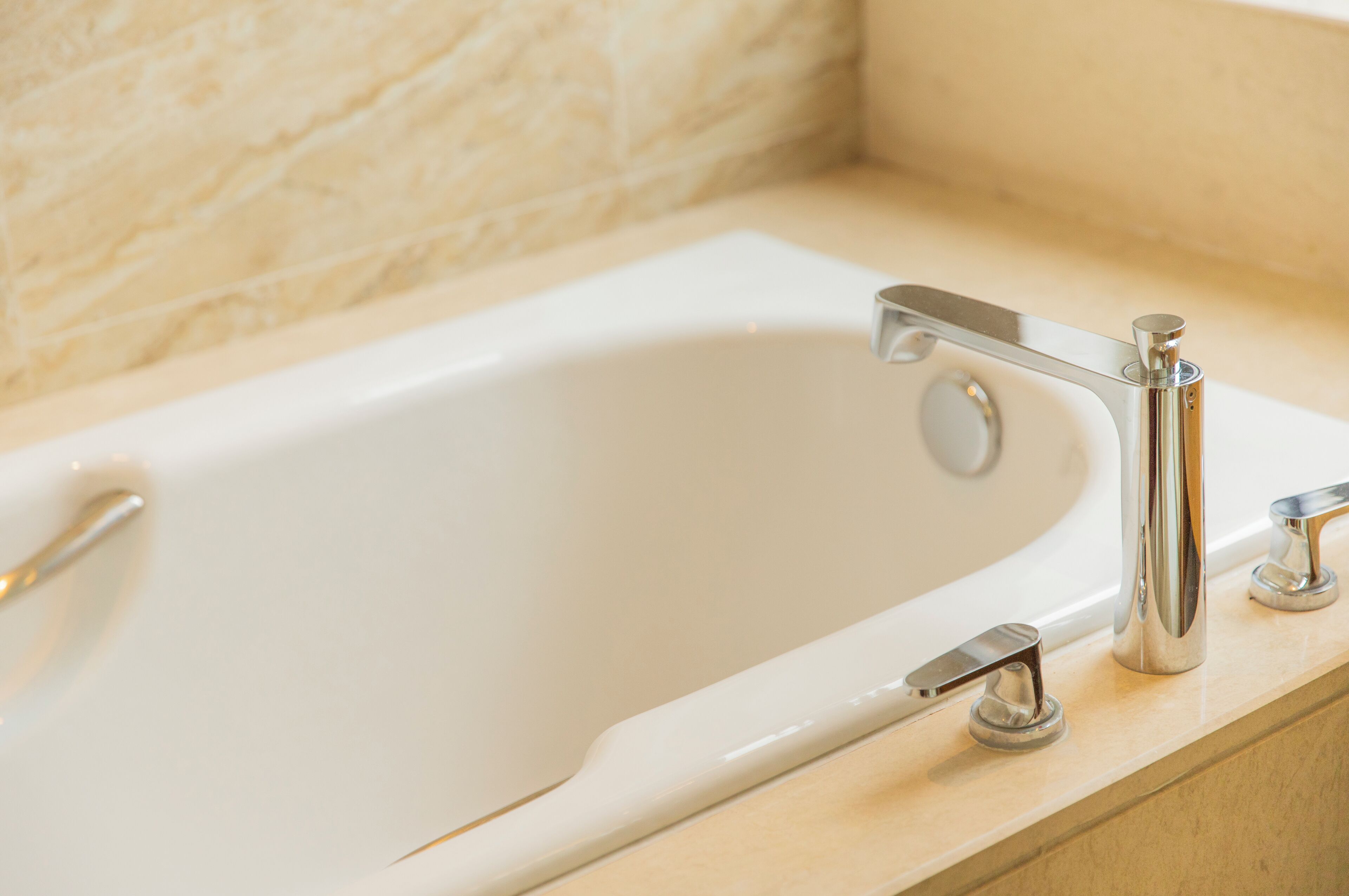 Una bañera blanca con accesorios de cromo en un baño con baldosas color crema.