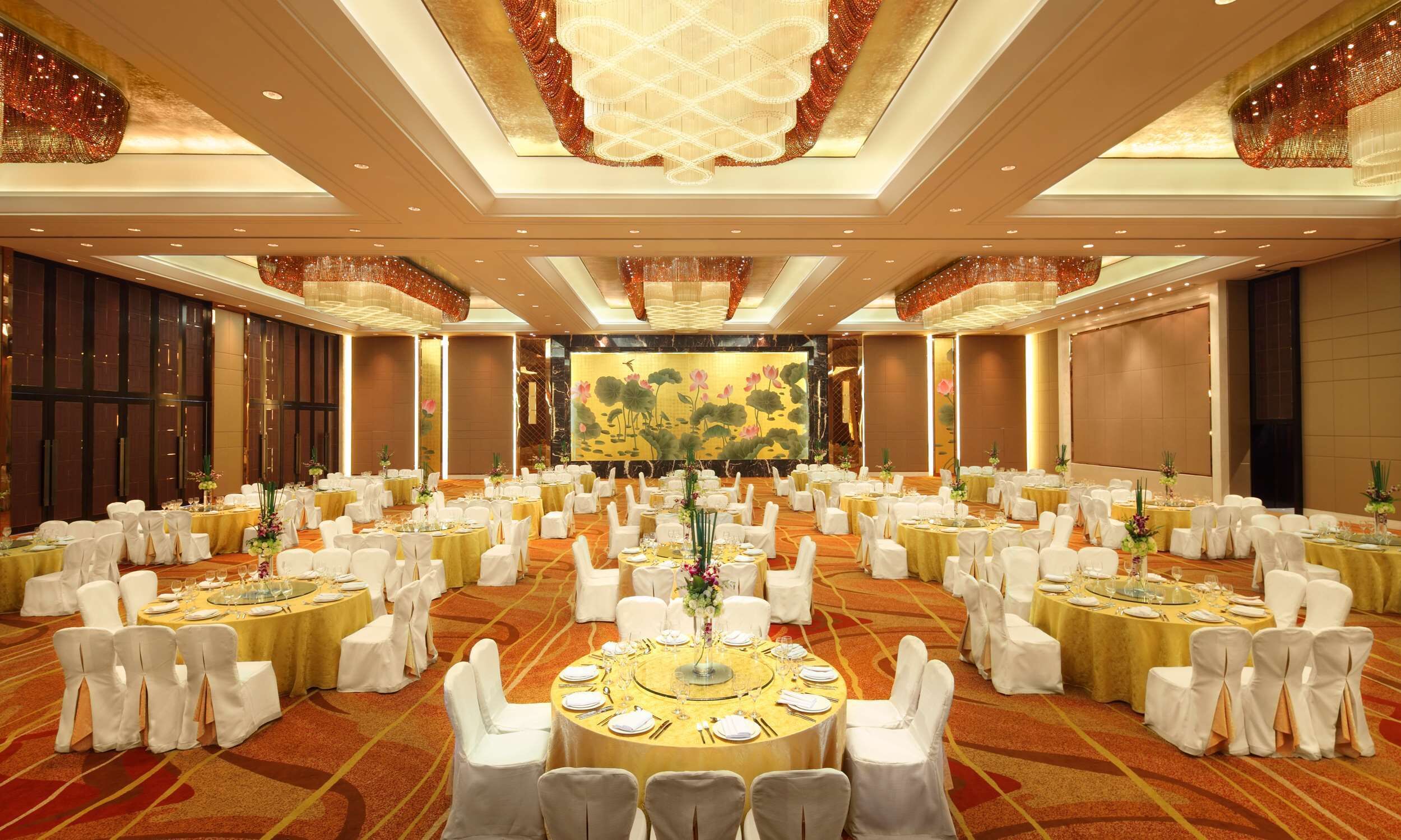 A large banquet hall with round tables, white chairs, and a large screen in the background.