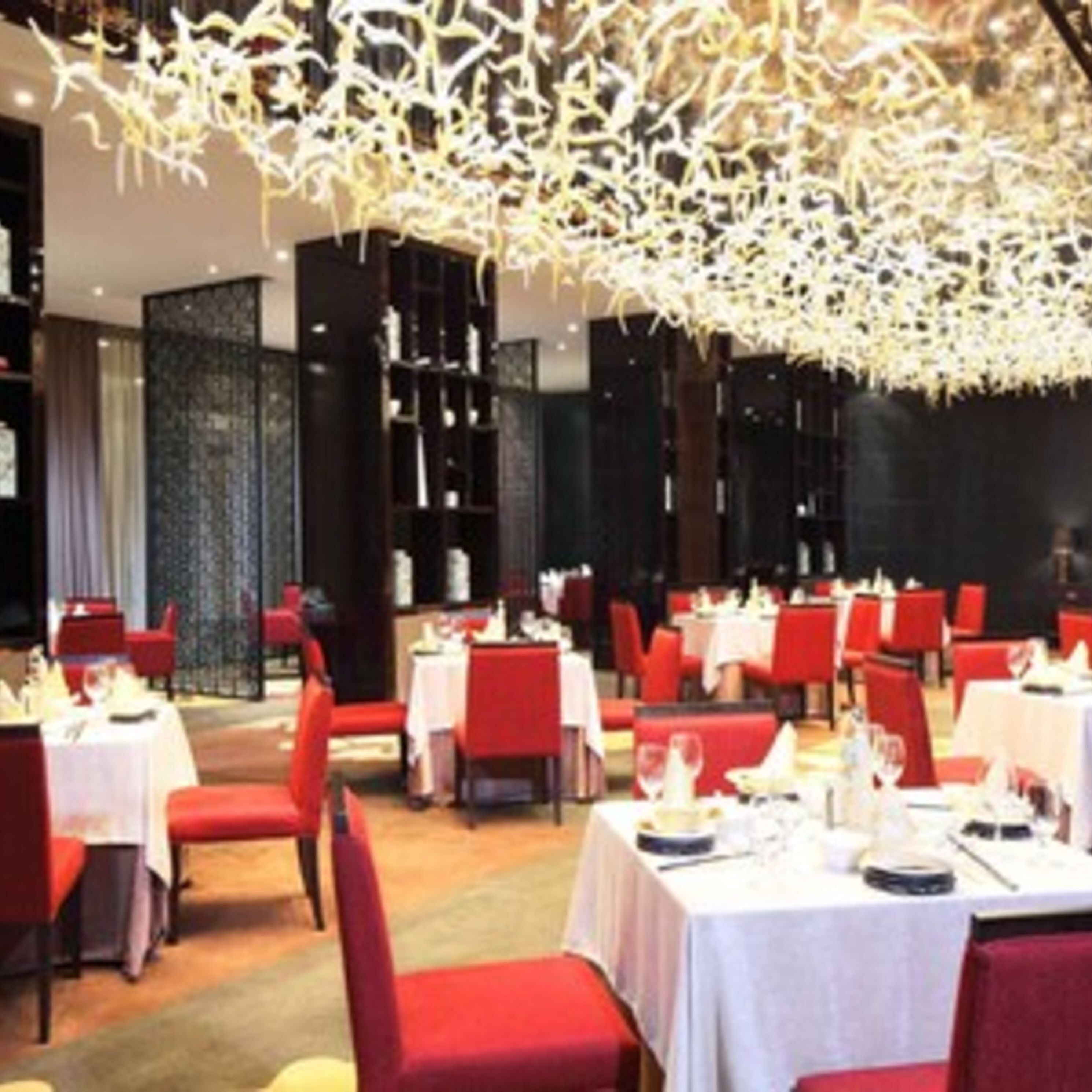 A restaurant with red chairs and white tables, a modern chandelier, and a dark interior.
