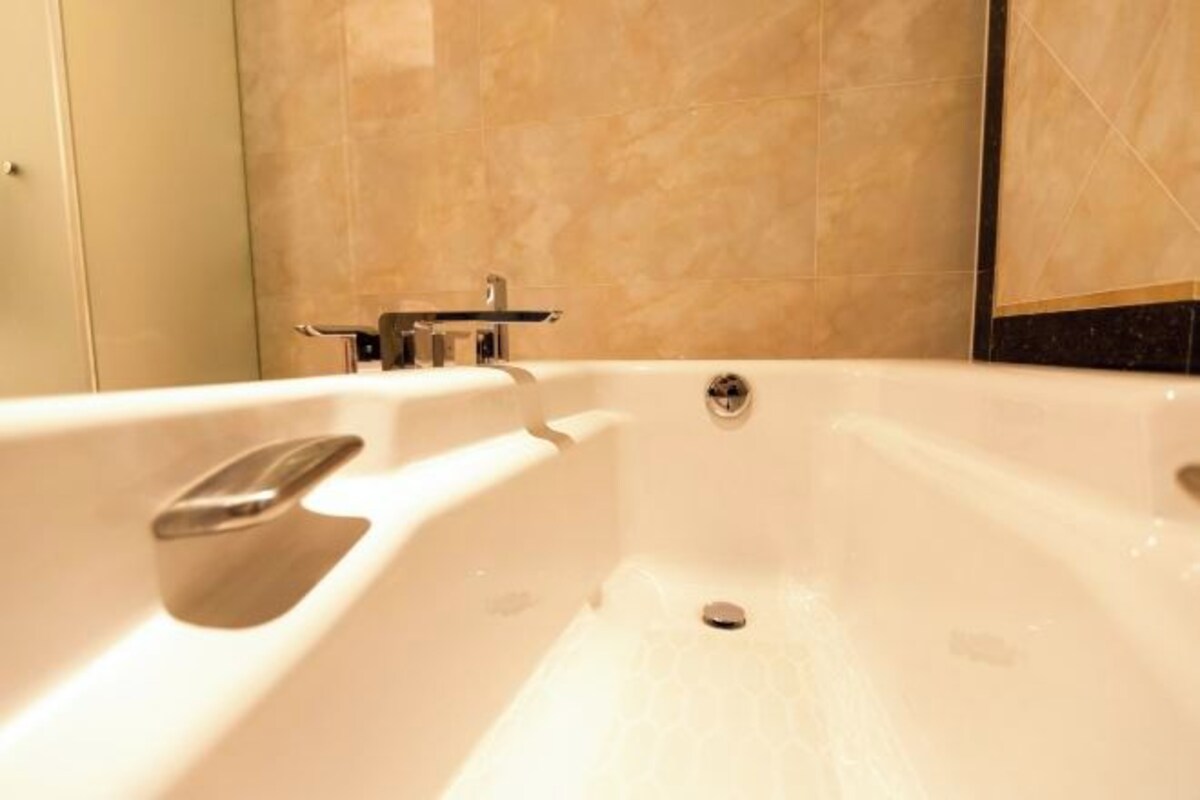 A large, white bathtub with a chrome faucet and a small shelf.