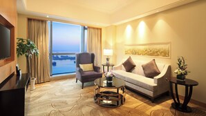 Habitación de hotel con un gran ventanal, televisor de pantalla plana, sofá, sillón y una mesa de centro.
