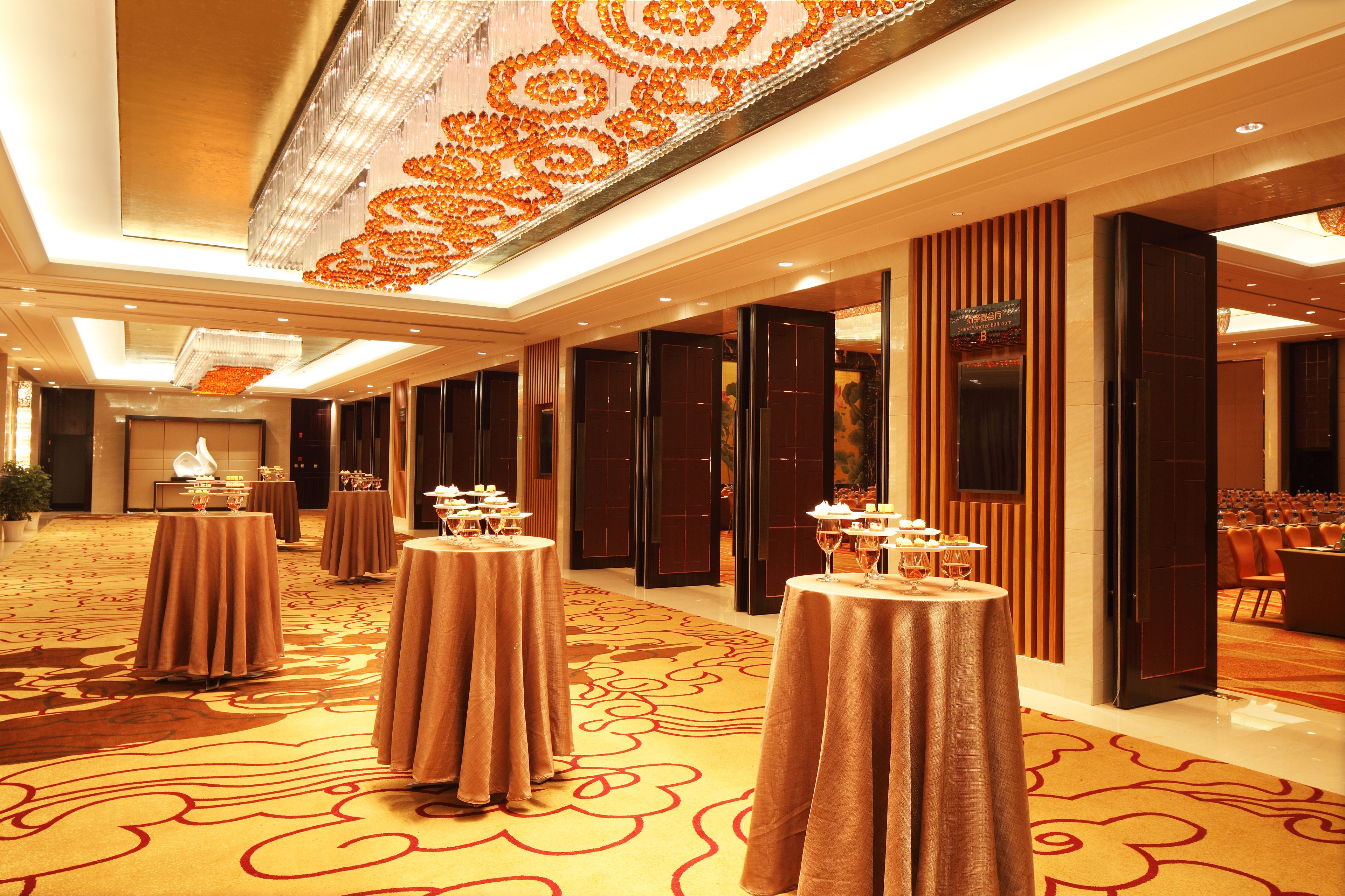 Un hall de hotel con varias mesas redondas dispuestas para comer, una lámpara de araña grande y suelo alfombrado.
