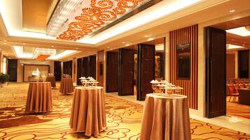 Un hall de hotel con varias mesas redondas dispuestas para comer, una lámpara de araña grande y suelo alfombrado.