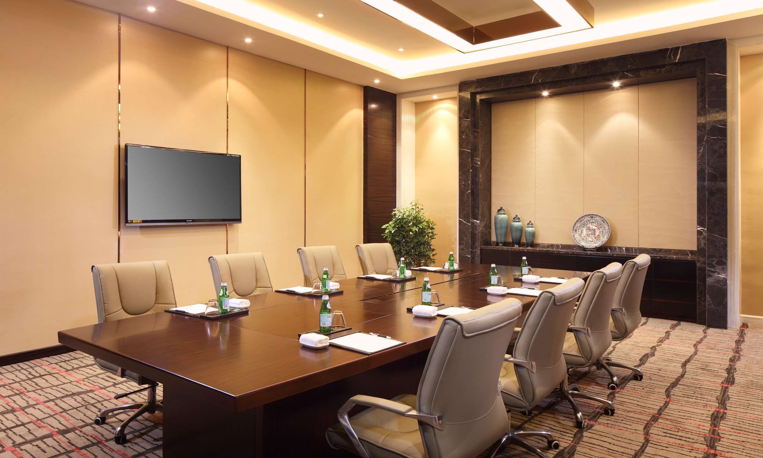 A conference room with a long table, chairs, a flat-screen TV, and decorative items.