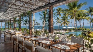 A covered outdoor dining area with tables set for two, overlooking a pool and palm trees. - Residences at Dorado Beach, a Ritz-Carlton Reserve (Dorado)