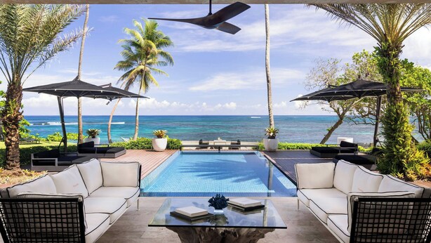 An outdoor pool area with a view of the ocean, surrounded by palm trees and furnished with white sofas and umbrellas. - Residences at Dorado Beach, a Ritz-Carlton Reserve (Dorado)
