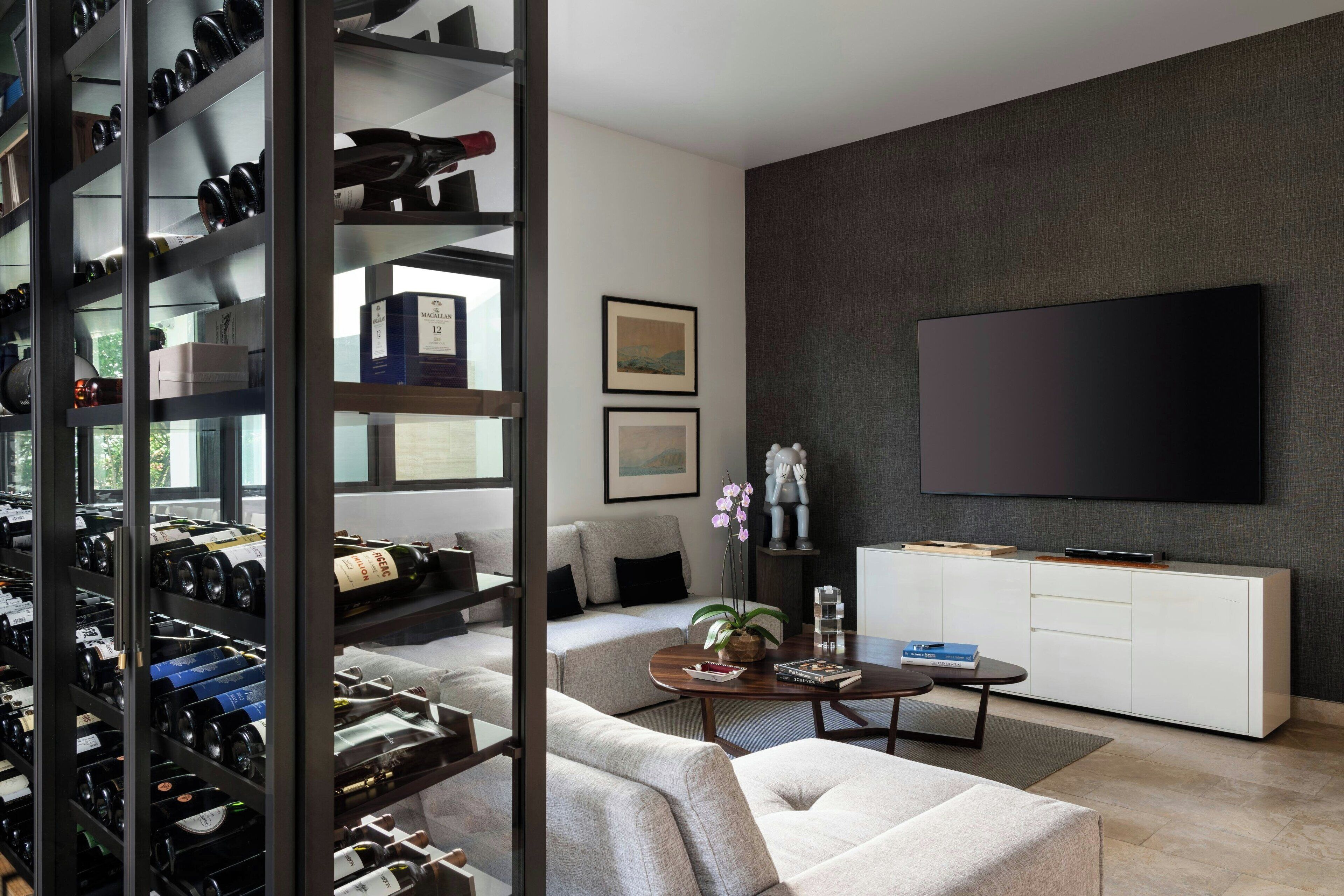 A modern living room with a wine rack, a sofa, a coffee table, and a TV on a grey wall.
