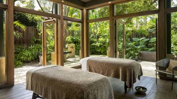 A room with two massage tables, large windows, and a view of a lush garden.