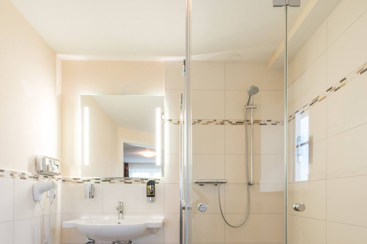 A bathroom with a glass shower enclosure, a sink, and a mirror.