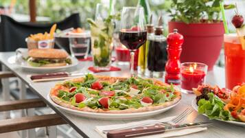 Een tafel met pizza, salade en drankjes, waaronder wijn en een cocktail.