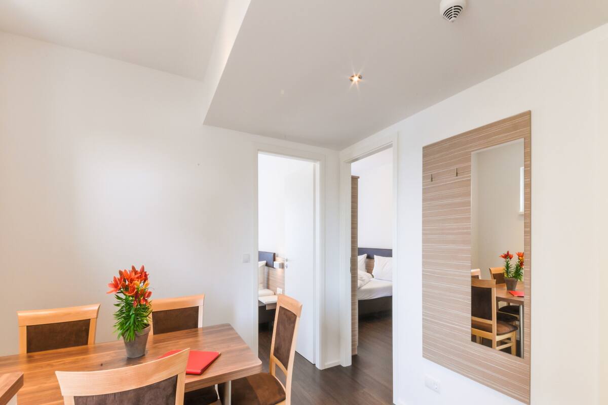 A modern dining area with wooden furniture, a potted plant, and a mirror on the wall.