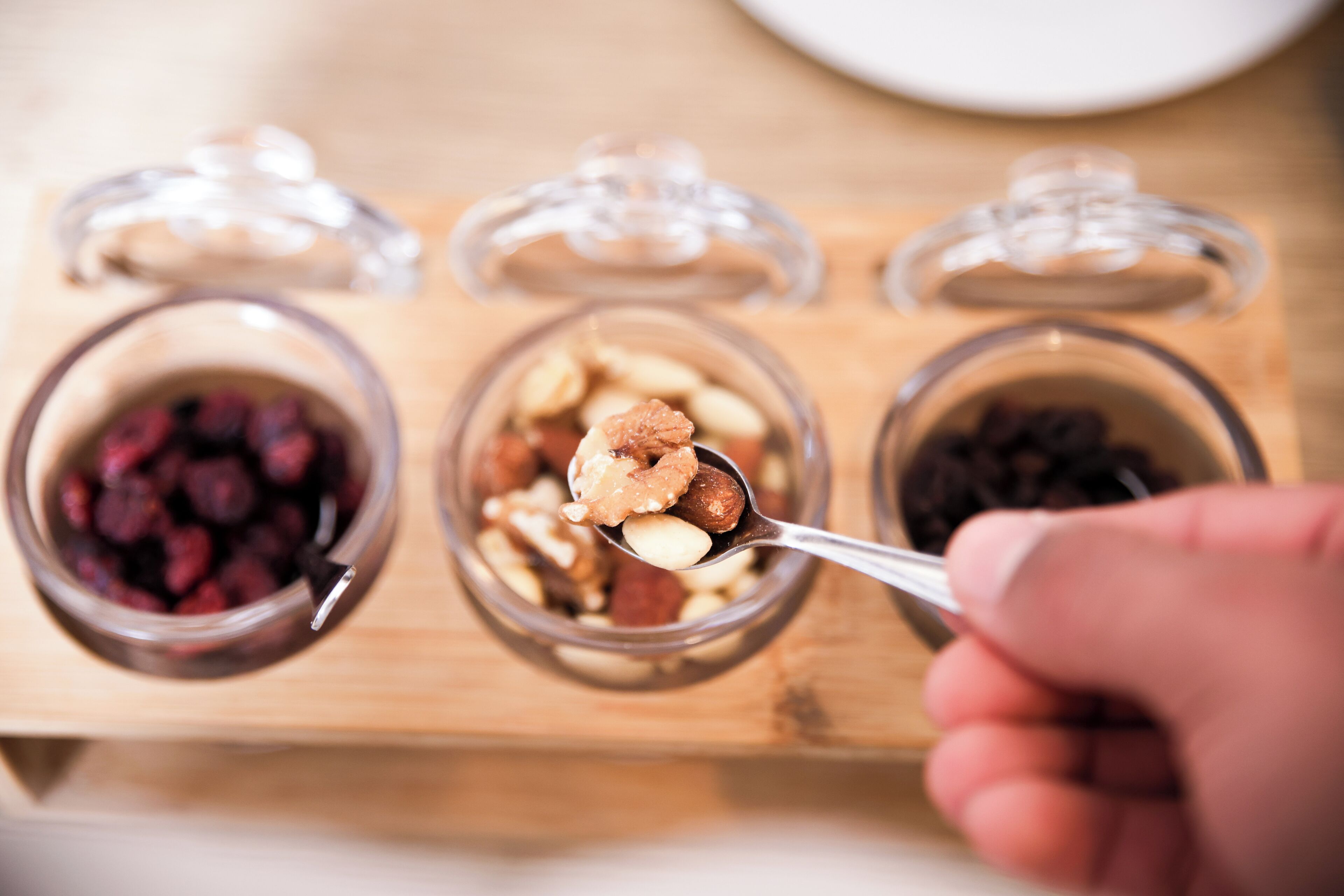 A hand holding a spoon with a mix of nuts and dried fruits.