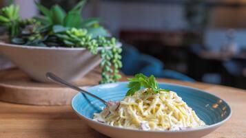 A bowl of pasta with a fork on a wooden table, with a potted plant in the background.