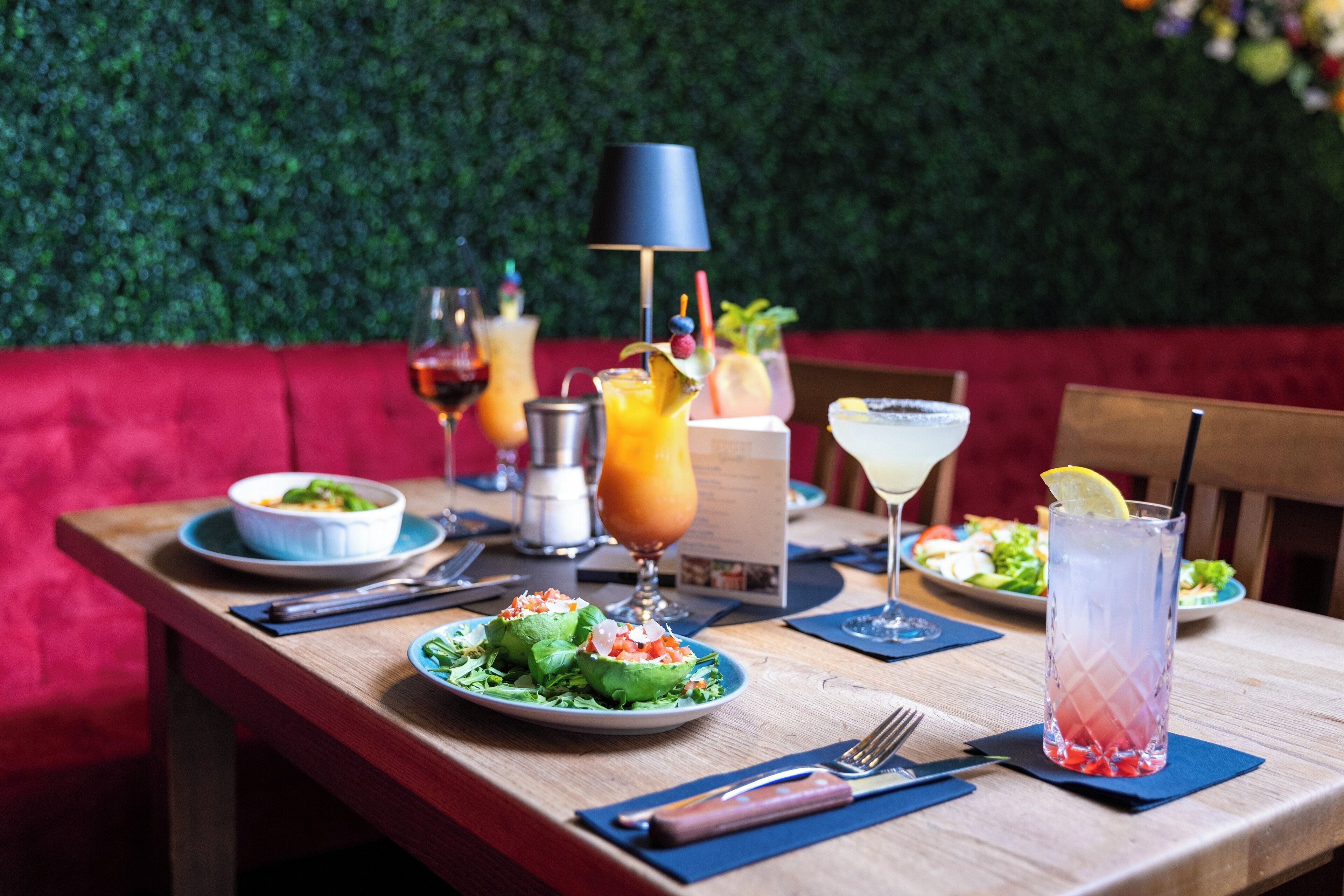 Une table à manger dressée avec différents plats et boissons, placée devant un mur vert et agrémentée de sièges rouges.