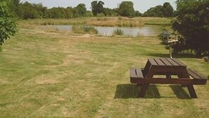 A picnic table in a grassy area with a pond and trees in the background. - Glebe Farm Apartments (Market Rasen)