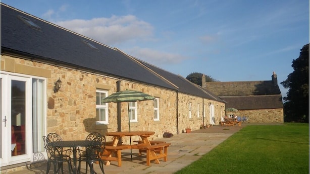 A stone building with a patio area featuring a table and chairs, a covered seating area, and a grassy lawn. - Hamsteels Hall (Durham)