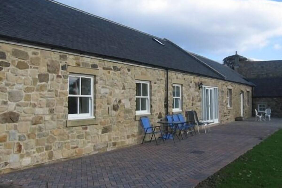A stone building with a paved patio and blue chairs.