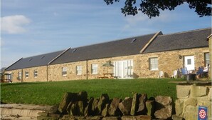 A stone building with a flat roof, a grassy lawn, and a stone wall in the foreground. - Hamsteels Hall (Durham)
