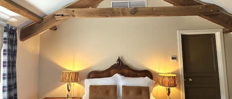 A bedroom with a wooden ceiling, a bed with white linens, two bedside tables with lamps, and a door.