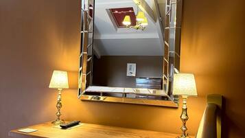A hotel room with a wooden desk, two lamps, a mirror, and a chair.