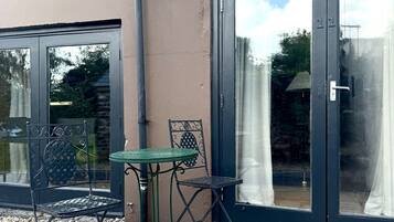 Eine Terrasse mit Tisch und zwei Stühlen, eine Steinsäule und eine große Glasdoor.