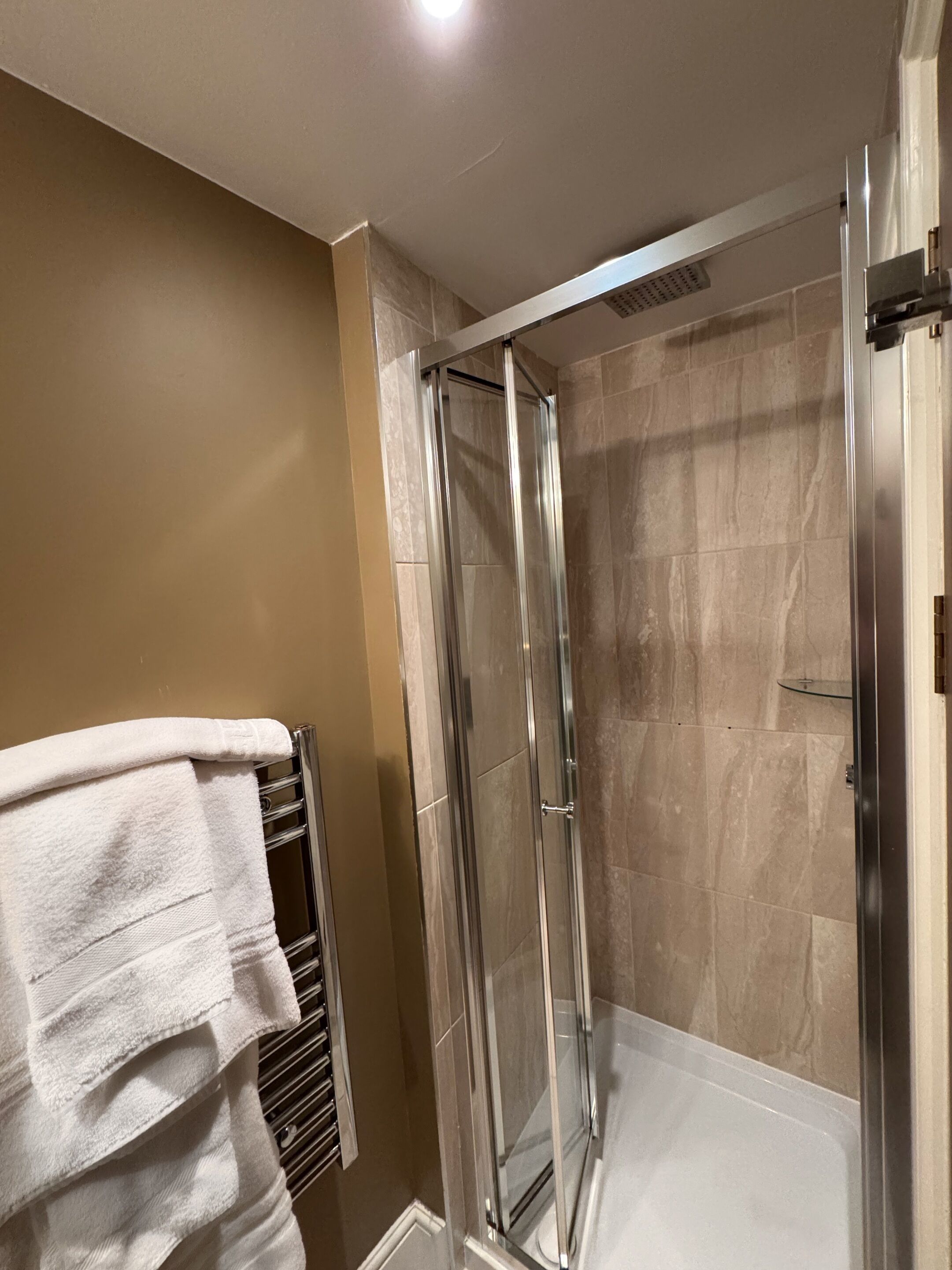 A modern bathroom with a glass-enclosed shower, beige tiles, and a white towel on a rack.