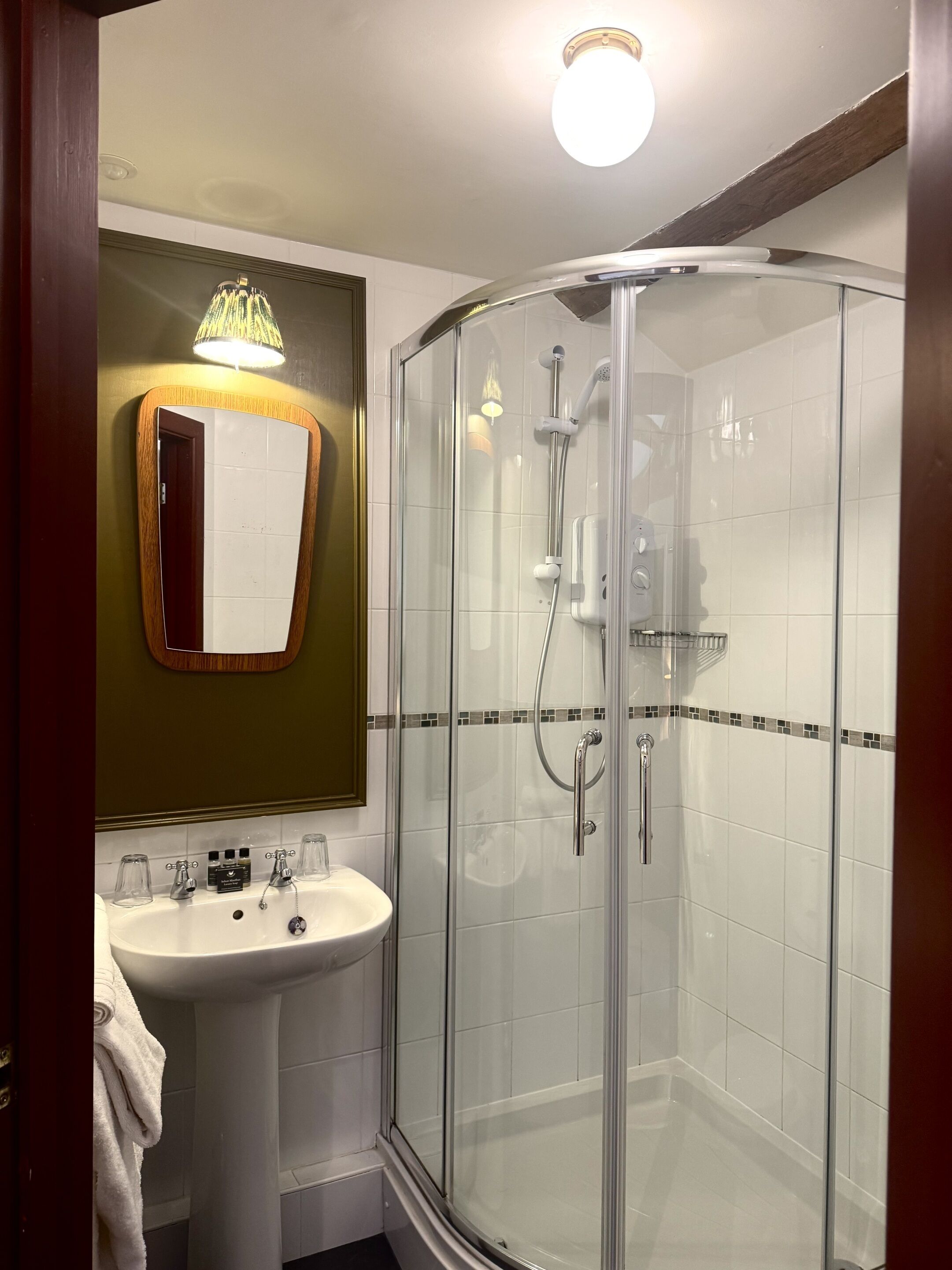 A bathroom with a glass-enclosed shower, a sink with a mirror, and a towel hanging on the wall.