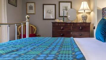 Un dormitorio con una colcha estampada, un aparador de madera con espejo, cuadros enmarcados en la pared y una almohada azul.