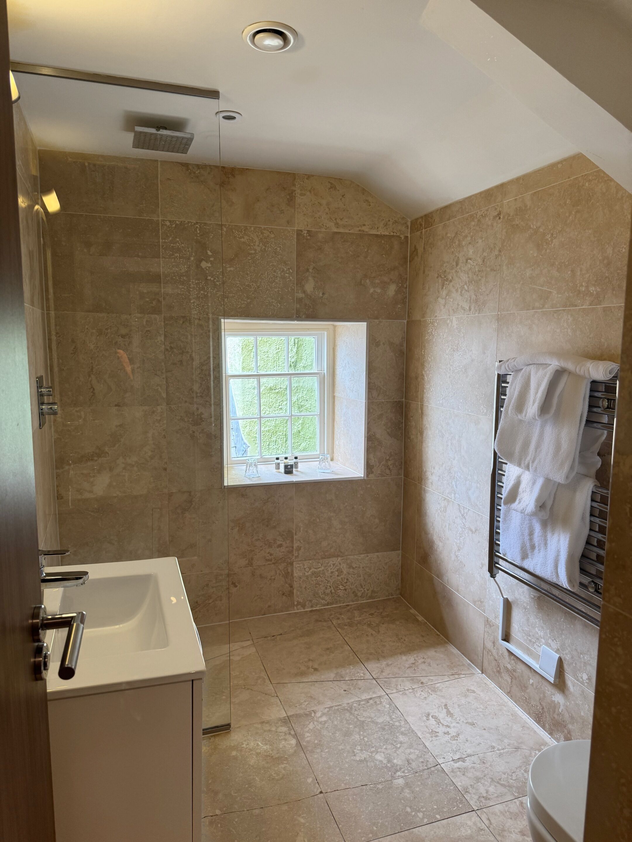 A modern bathroom with a walk-in shower, a window, a towel rack, and a sink.