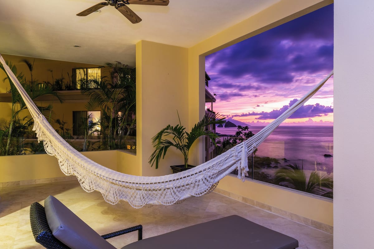 A hammock on a balcony with a view of the ocean at sunset.