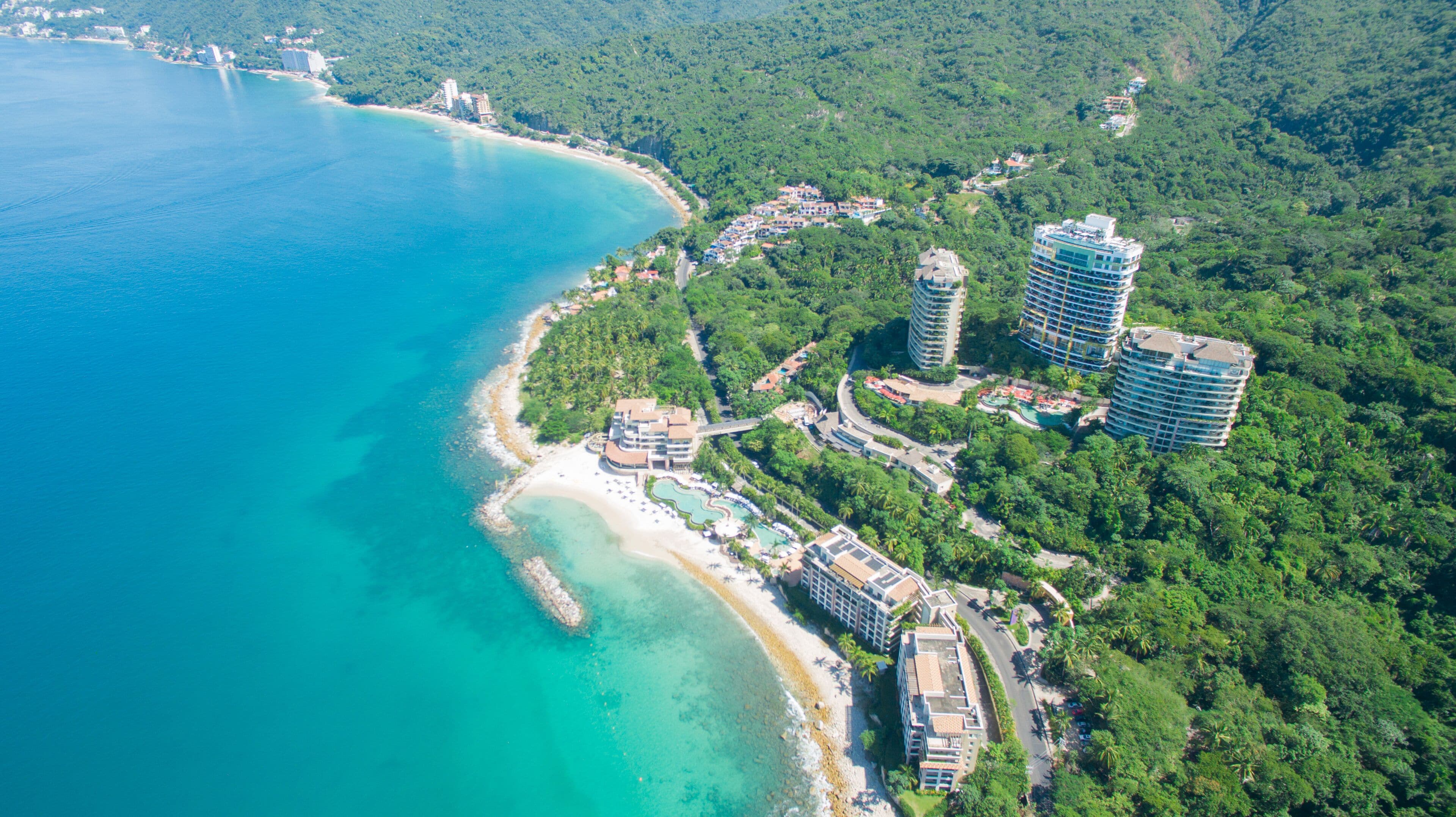 An aerial view of a coastal resort with beachfront properties, a swimming pool, and lush greenery.