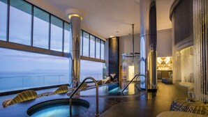 Un área de piscina interior lujosa con vistas despejadas al océano, asientos cómodos y una decoración elegante.
