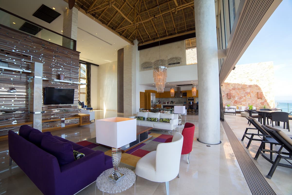 A spacious living area with a modern design, featuring a large flat-screen TV, comfortable seating, and a view of the ocean.