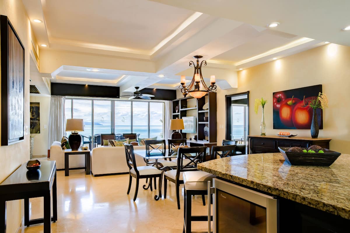 A spacious kitchen with a large island, dining area with chairs, and a view of the ocean.
