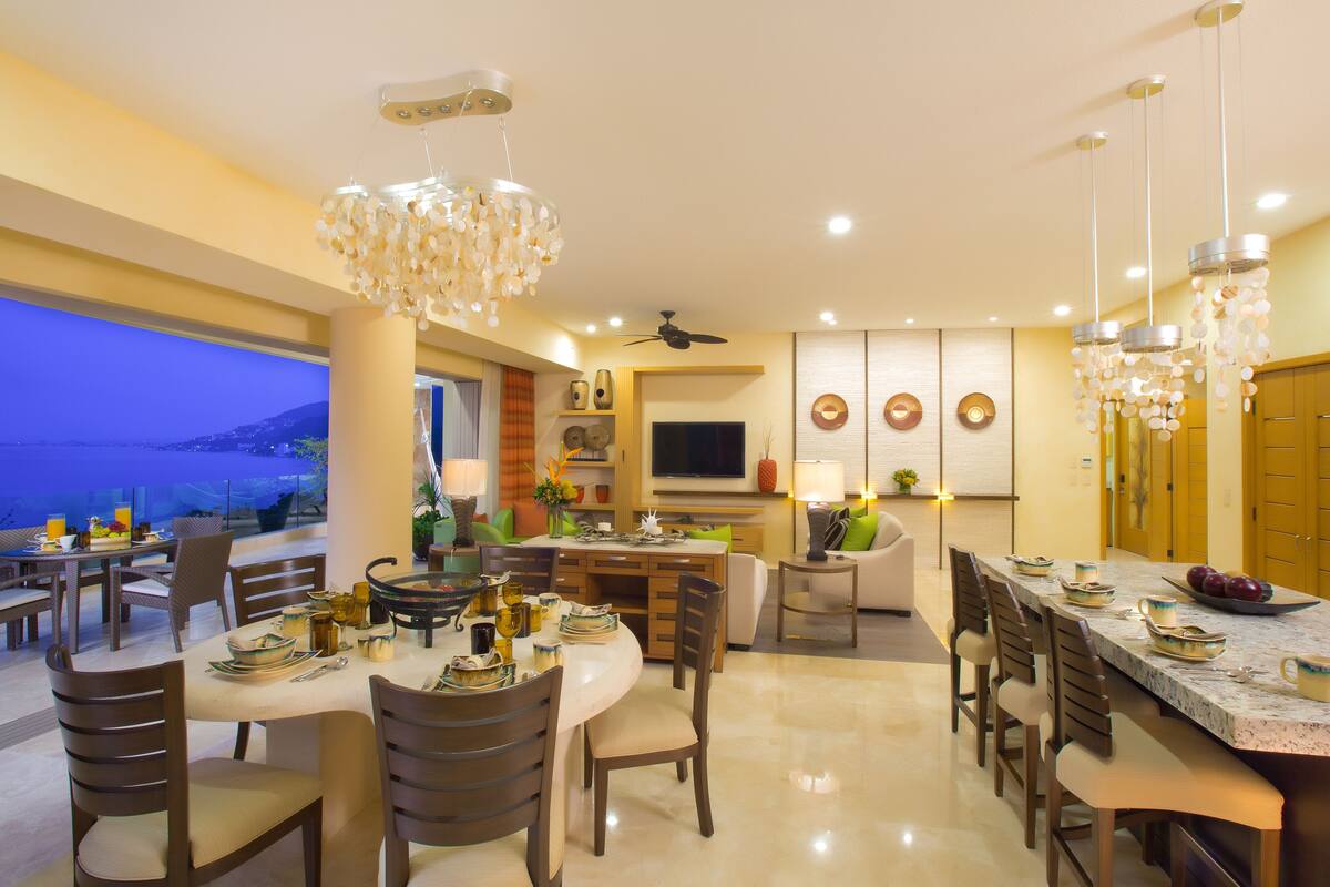 A modern dining area with a large island, multiple seating arrangements, and decorative lighting.