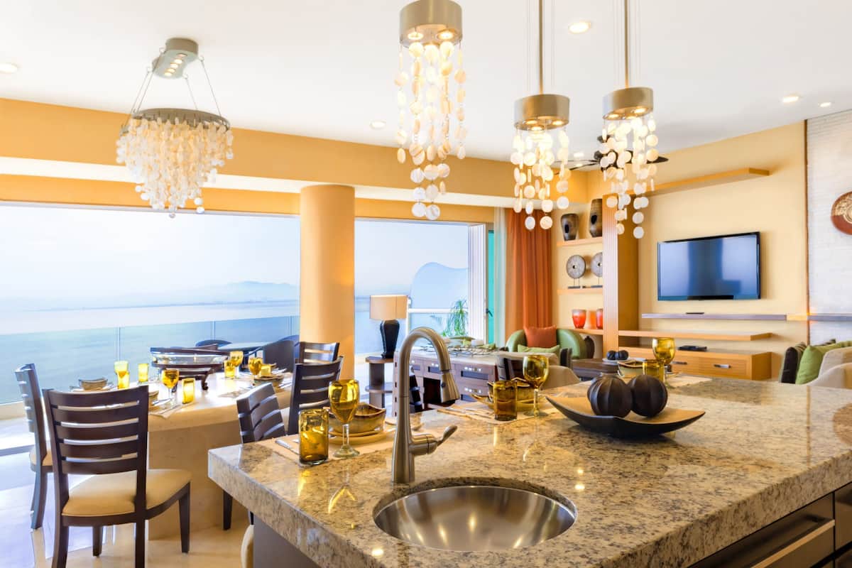 A modern kitchen with a large island, stainless steel sink, and overhead lighting.