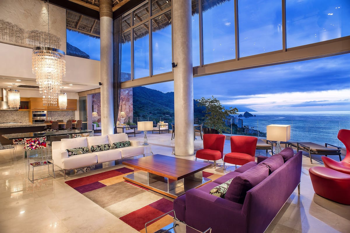 A spacious living area with a large window overlooking a scenic view, a modern chandelier, and contemporary furniture.