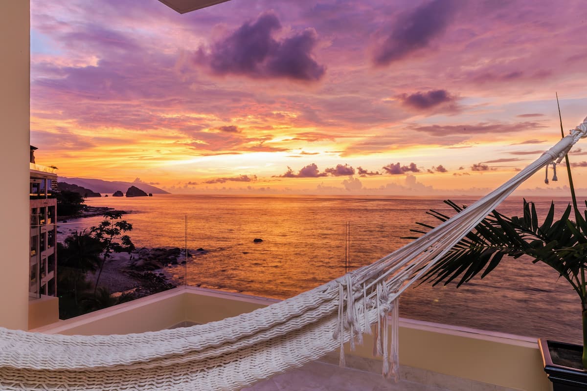 A hammock on a balcony overlooking a sunset over the ocean.