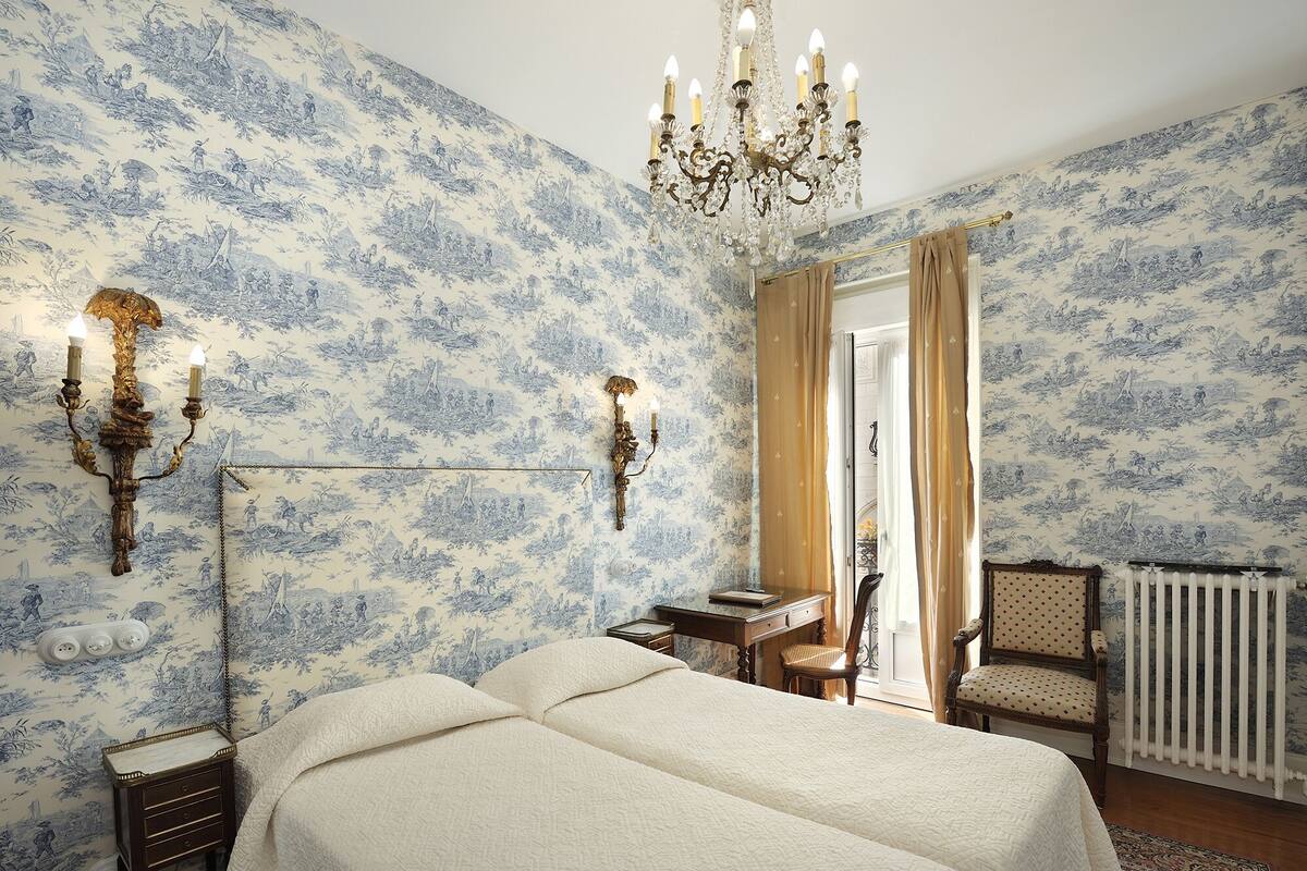 Ein Schlafzimmer mit zwei Betten, einer Kandelaber, Wandleuchten, einem Schreibtisch und einem Stuhl.