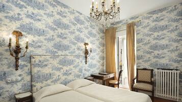 Quarto com duas camas, um candelabro, arandelas, uma escrivaninha e uma cadeira.