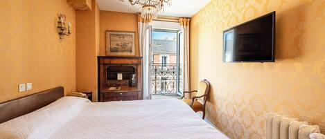 Habitación de hotel con una cama grande, un televisor montado en la pared, una araña y vistas al balcón exterior.
