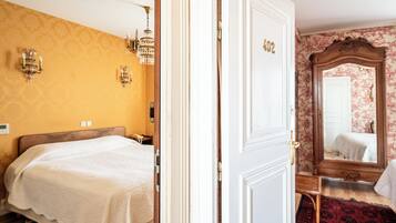 A hotel room with a bed, a door with a number, a mirror, and a patterned wall.